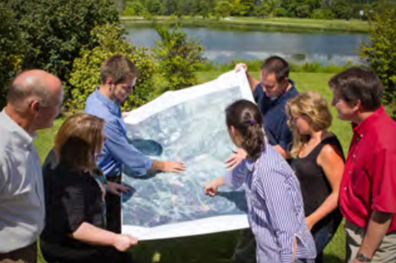 Healthy Community Connections Photo of community members by pond, looking at map/blueprint