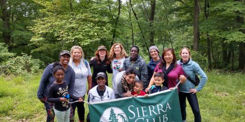 Group of women and children holding up Sierra Club banner while out in the forest